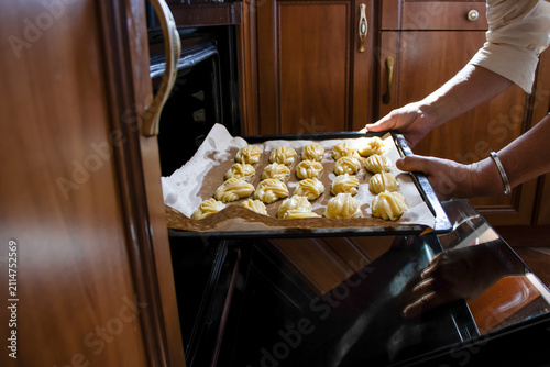 A woman places a baking sheet of choux pastries into the oven.