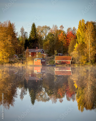 фотографія Traditional red Swedish houses and colorful autumn forest reflecting on the calm, mirror-like water surface of a peaceful lake