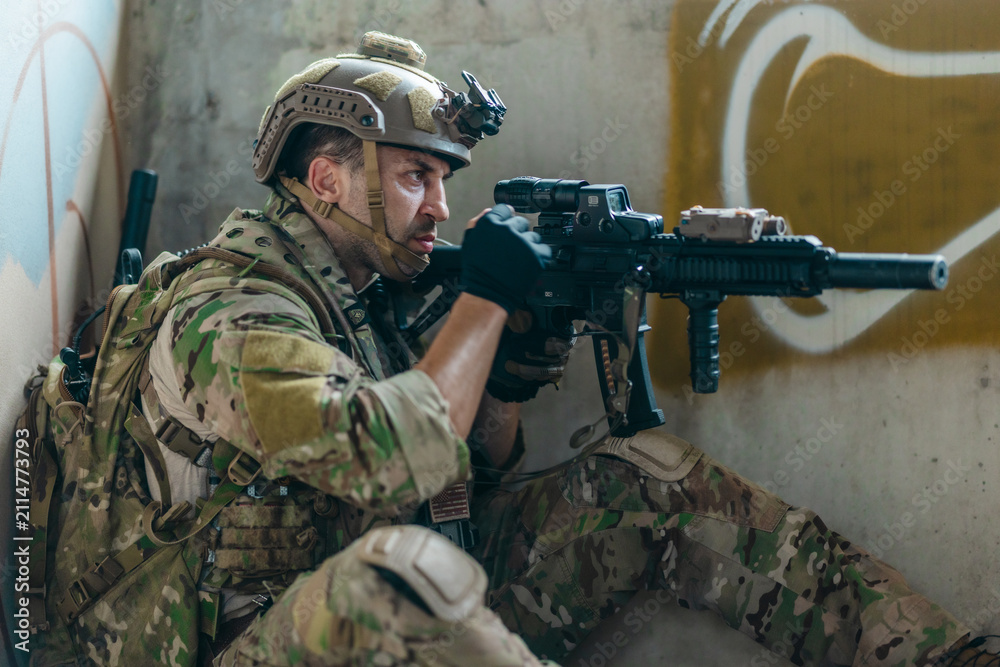 Fototapeta premium Military tactical operator holds rifle while clearing abandoned concrete building interior