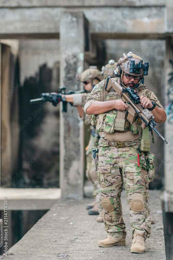 Fototapeta premium Military tactical operator holds rifle while clearing abandoned concrete building interior