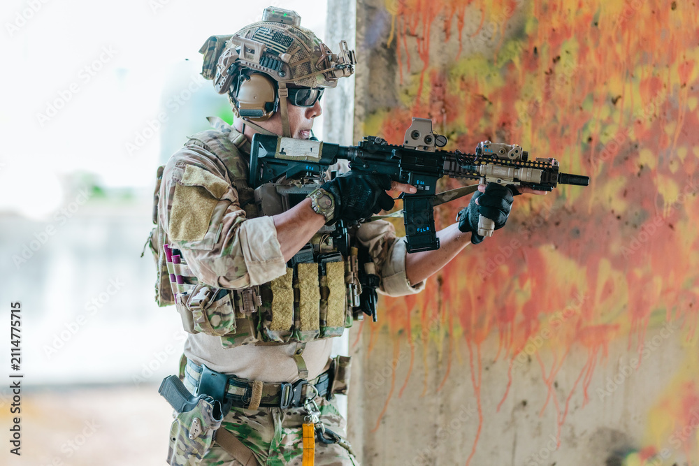 Fototapeta premium Military tactical operator holds rifle while clearing abandoned concrete building interior