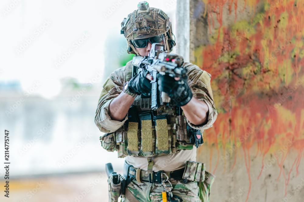 Fototapeta premium Military tactical operator holds rifle while clearing abandoned concrete building interior