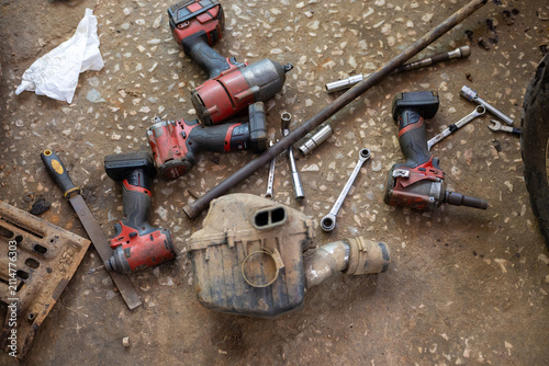 Fotografie Worn pneumatic impact wrenches and scattered sockets on workshop floor next to d