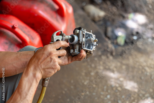 Fotografie Mechanic holding and cleaning small carburetor with air blow gun, hands showing