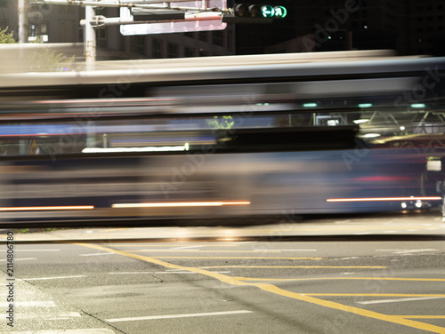 Long-exposure motion blur of a city bus passing through an urban intersection at night with light trails and road markings.