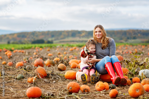 Little preschool girl and young mother on pumpkin patch with lots of pumpkins in autumn field. Happy child and woman, family enjoying harvest season outdoors. Real life, real people.