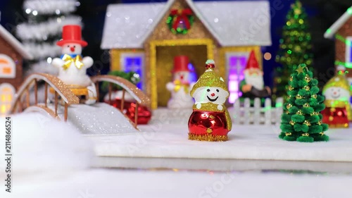 Toy yellow car carrying a Christmas tree on roof through miniature winter village