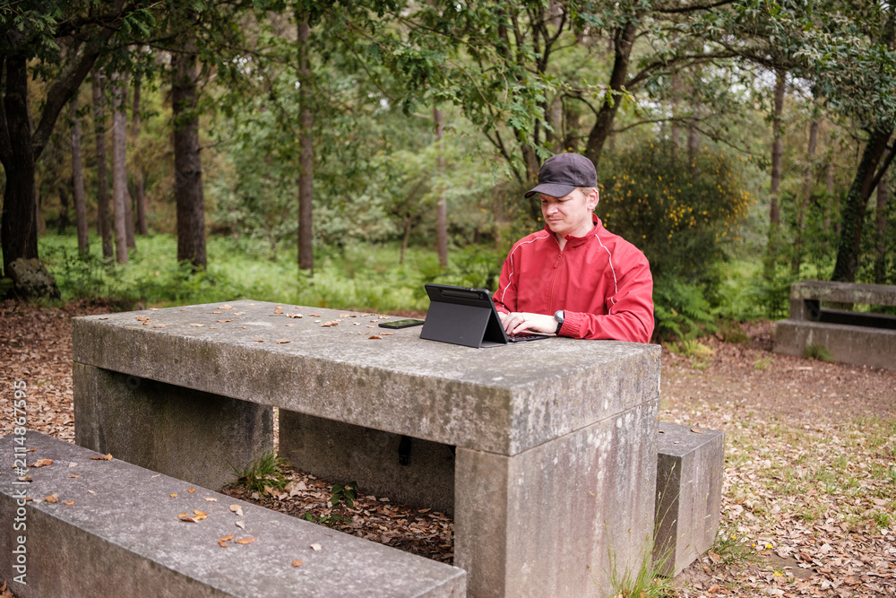 Fototapeta premium Man working remote on laptop at forest picnic table