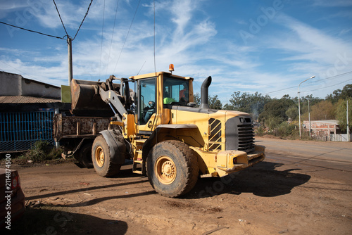 Fotografie Front wheel loader lifting bucket over tipper truck at outdoor construction zone