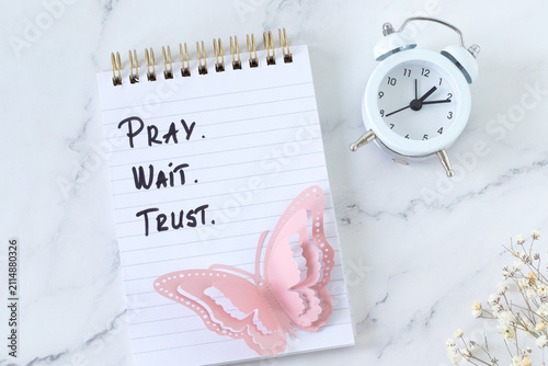 Pray, wait, trust, christian inspirational text in a notebook with alarm clock. Biblical concept of patience and faith in God Jesus Christ.