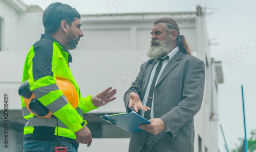 Angry businessman arguing with engineer over problem at house construction site outdoors