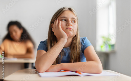 Fotografie Bored schoolgirl resting her face on one hand and looking away from open noteboo
