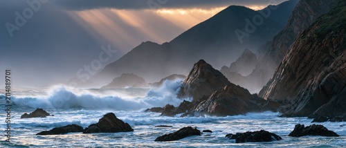 Dramatic ocean waves crashing on rocky coast. Stormy sea landscape with golden sun rays.