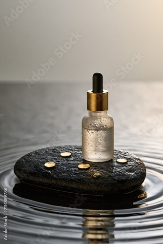 Serum bottle on a stone in water. Cosmetic oil dropper for skincare and beauty treatment.