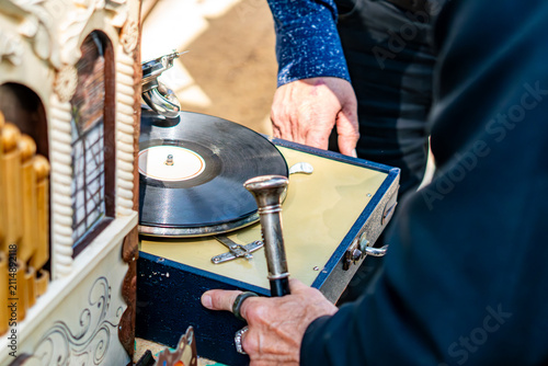 Obraz na plátně Close-up of a retro portable suitcase gramophone with a black vinyl record being operated by a man at an outdoor flea market
