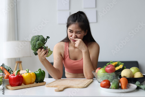 Картината върху платно Young woman disliking broccoli while preparing healthy food.