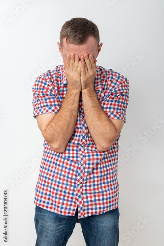 Upset young man with head in hands, covering his face in distress on a plain background, conveying sadness, frustration, shame and emotional overwhelm