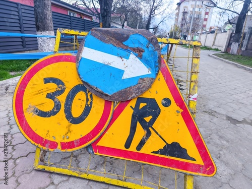 Road construction safety signs with speed restriction and directional arrow beside residential sidewalk during municipal utility maintenance project