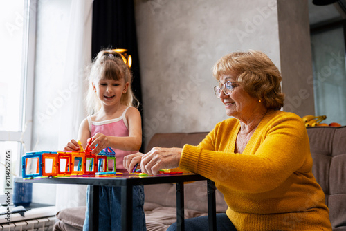 Quadro su tela Granddaughter and grandmother playing with colorful magnetic blocks