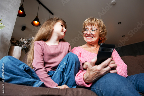 Fotografie Grandmother and girl enjoying smartphone together at home