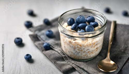 creamy overnight oats topped with fresh blueberries in a glass jar placed on a gray napkin with a spoon beside it