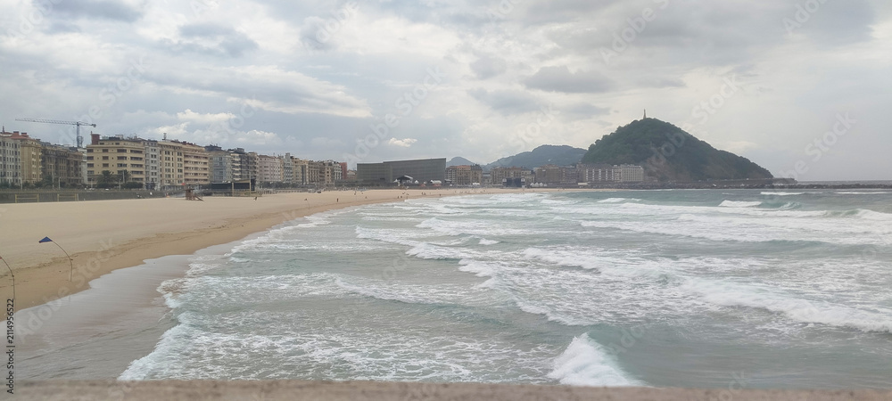 Fototapeta premium Vista general de la costa y la ciudad bajo cielo nublado en San Sebastián, España