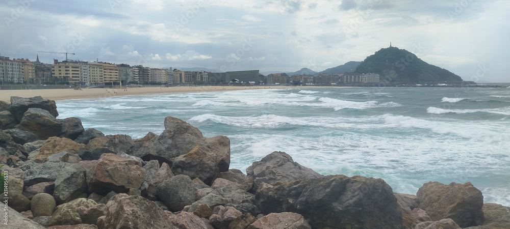 Fototapeta premium Vista general de la costa y la ciudad bajo cielo nublado en San Sebastián, España