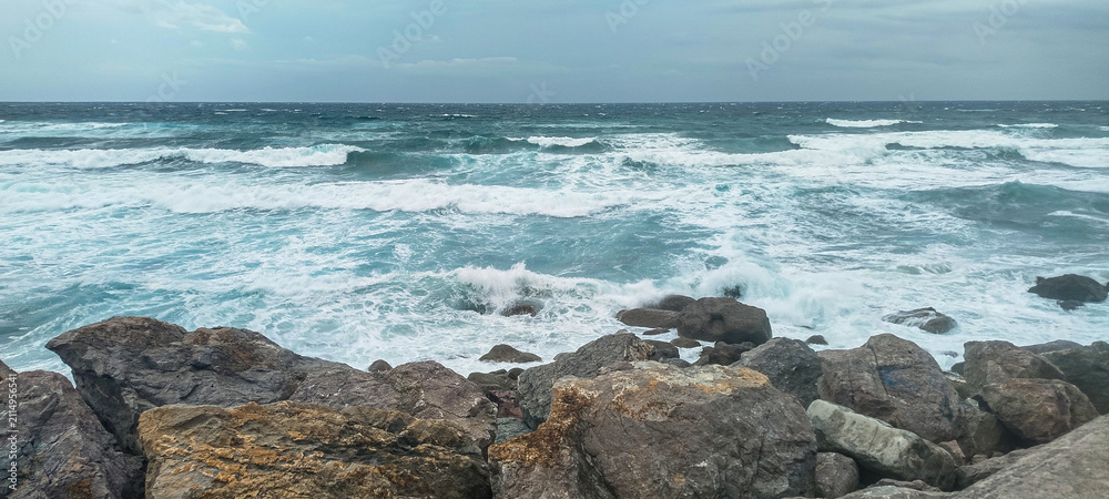 Fototapeta premium Olas rompiendo contra rocas en la costa marina bajo nubes