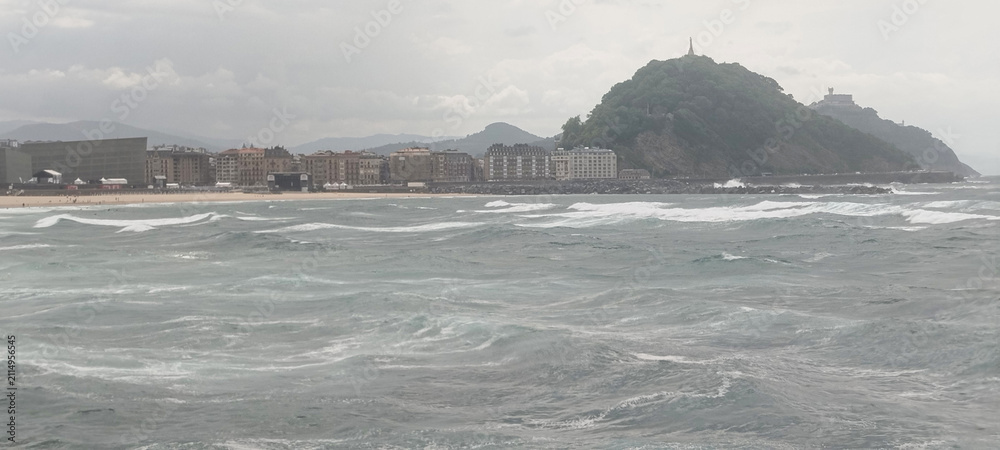 Fototapeta premium Vista general de la costa y la ciudad bajo cielo nublado en San Sebastián, España