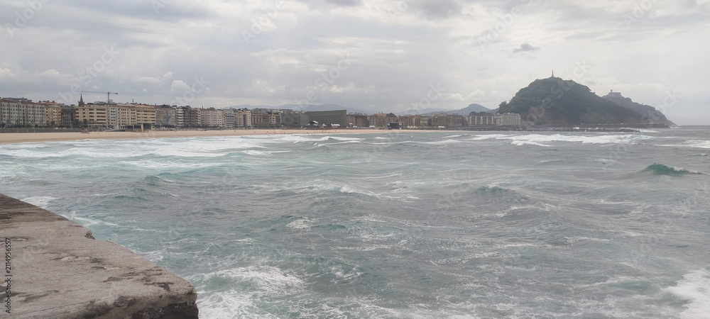 Fototapeta premium Vista general de la costa y la ciudad bajo cielo nublado en San Sebastián, España