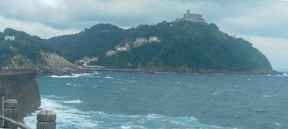 Fototapeta premium Vista panorámica de la bahía y la costa marítima bajo cielo nublado en San Sebastián, España.