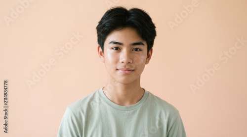 A young man with short black hair, wearing a light green t-shirt, standing against a plain beige background.