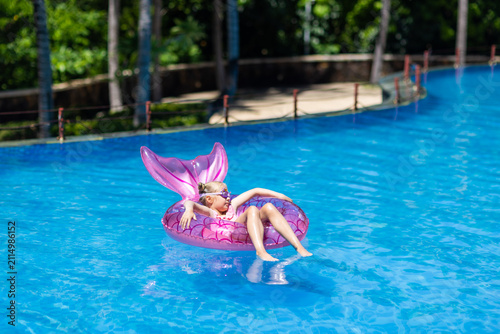 Quadro su tela Young girl relaxing on a pink inflatable float in a swimming pool