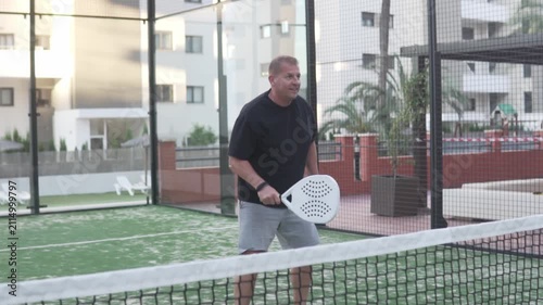 Senior male athlete playing padel on an outdoor court in a modern residential area. Active lifestyle, recreational sport, fitness, competition and healthy aging concept