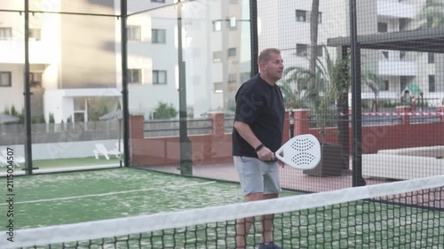 A man playing padel on an outdoor court, returning the ball with a racket near the net. Active lifestyle, recreational sport and fitness concept
