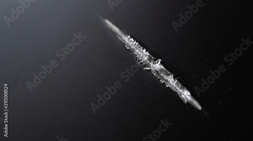 A close-up view of a textured scratch or crystalline formation on a dark surface, highlighting intricate details.