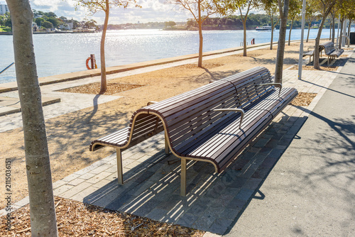 Empty stylish wooden benches along a footpath lined with trees in a waterfront park on a sunny autumn day