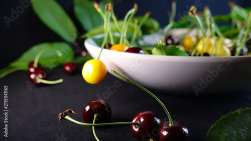 Quadro su tela Freshly picked yellow and dark red wild cherries, some in a white bowl and some
