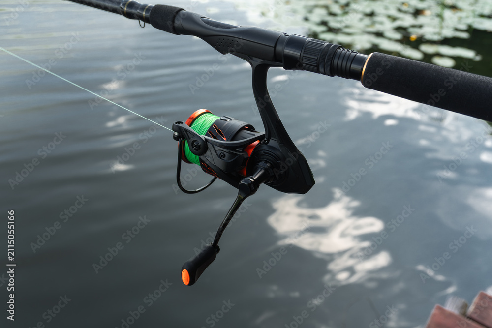 Fototapeta premium Fishing rod and spinning reel closeup, angler tackle equipment, active sportfishing gear and line over lake water.