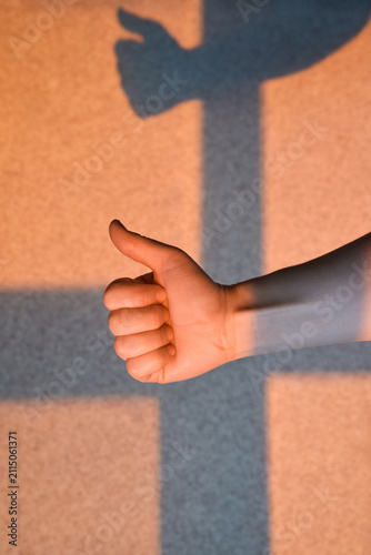 Canvas Print Hand Showing Thumbs Up In Warm Light Against Textured Wall With Tall Shadow Above