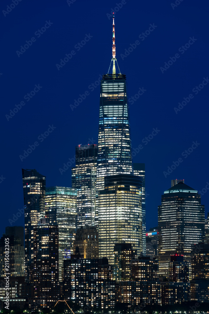 Obraz premium Vertical night view of downtown Manhattan featuring brightly lit high rise skyscrapers against a deep blue evening sky in New York.