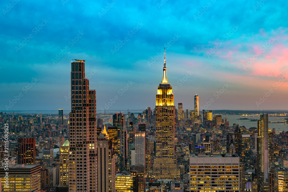 Obraz premium Stunning panoramic view of the Manhattan skyline in New York during dusk, featuring illuminated skyscrapers against a vibrant twilight sky.
