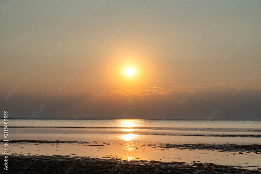 Fototapeta premium Golden sunset over Lake Constance viewed from the scenic shore of Rohrspitz in Vorarlberg, Austria, with calm water and serene beach details