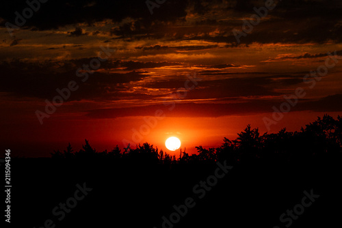Fiery sunset above silhouetted forest beneath dramatic storm clouds