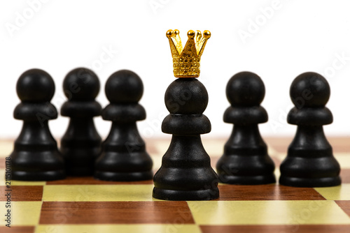 A chess pawn wearing a gold crown, set against a background of ordinary chess pawns.