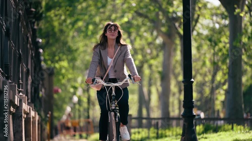 Video of smiling woman riding a bicycle through the park.