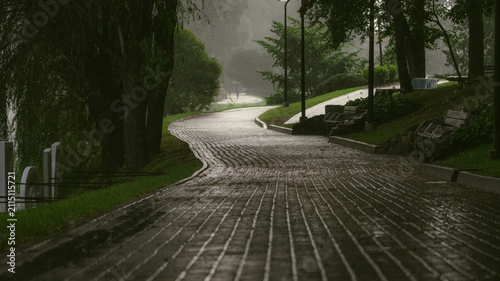 Heavy rain falls on an empty riverside park path