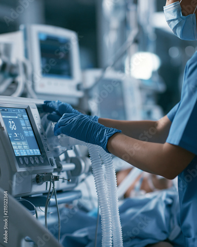 Nurse in ICU monitoring patient with respiratory equipment and vital signs in hospital during emergency care