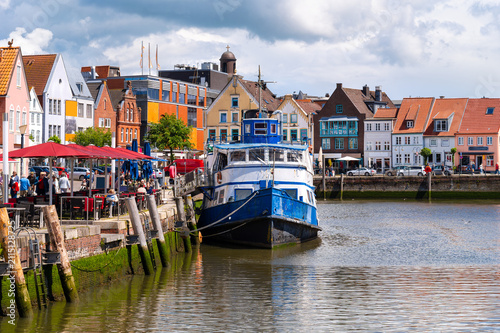 Obraz na plátně Historic harbor of Husum with an ship, waterfront restaurants and colorful old town beneath dramatic clouds on Germany's North Sea coast