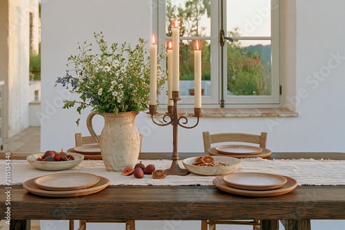 Tuscan dining tablescape featuring dark oak table, floral centerpiece, candles, and rustic dishware, set for evening meal with natural light and scenic view